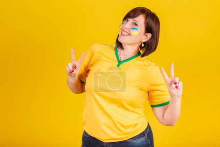 Foto de Mujer pelirroja, fan del fútbol brasileño. signo de la suerte, dedos de la paz y el amor, buenas vibraciones. - Imagen libre de derechos