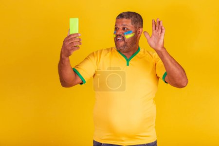 Foto de Hombre negro brasileño, fanático del fútbol de Brasil. videollamada, videoconferencia. smartphone - Imagen libre de derechos