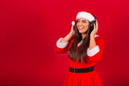 Photo for Beautiful Brazilian woman dressed in Christmas clothes, Santa Claus. listening to music in headset. - Royalty Free Image
