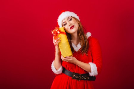 Téléchargez les photos : Belle femme rousse brésilienne, vêtue de vêtements de Noël, le Père Noël. étreinte cadeau jaune. - en image libre de droit