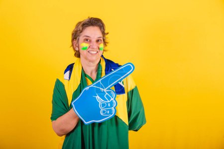 Photo for Adult adult woman, brazil soccer fan, smartphone, with foam finger, pointing right. - Royalty Free Image