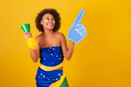 Photo for Young black woman brazilian soccer fan. with horn and foam finger, cheering. - Royalty Free Image