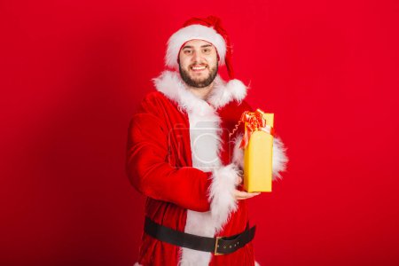 Photo for Caucasian, Brazilian man dressed in Christmas outfit, Santa Claus. holding yellow gift. - Royalty Free Image