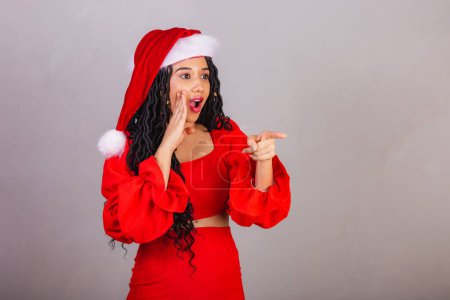 Photo for Brazilian black woman, wearing christmas clothes, merry christmas, smiling, surprised pointing at something. - Royalty Free Image