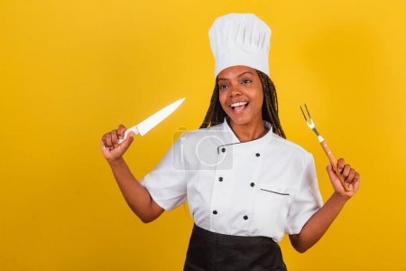 Téléchargez les photos : Jeune femme afro brésilienne, chef cuisinier, tenant couteau et fourchette pour barbecue, se préparant à cuisiner. - en image libre de droit