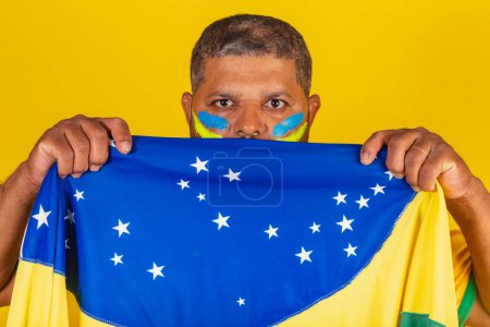 Téléchargez les photos : Homme noir brésilien, fan de football brésilien. gros plan photo couvrant le visage avec le drapeau brésilien. - en image libre de droit