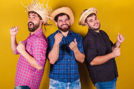 Foto de Tres amigos vistiendo ropa típica para la Festa Junina. Bailando, de fiesta. - Imagen libre de derechos