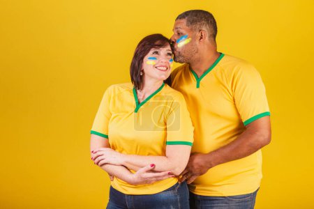 Photo for Couple, red-haired woman and black man, Brazilian soccer fans. Arms crossed, smiling at the camera. - Royalty Free Image