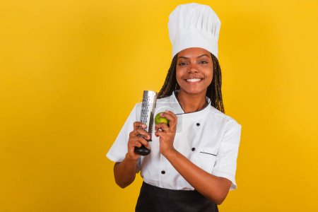 Téléchargez les photos : Jeune femme afro brésilienne, chef cuisinier, tenant citron et râpe pour la cuisine. - en image libre de droit