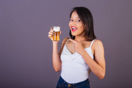 Foto de Mujer adulta joven del noreste de Brasil. indicando cerveza, apuntando al vaso de cerveza. - Imagen libre de derechos