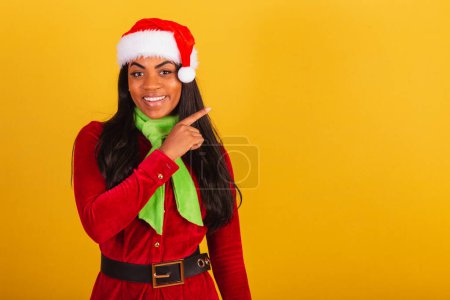 Téléchargez les photos : Belle femme brésilienne noire, vêtue de vêtements de Noël, Père Noël claus, présentant le produit ou le texte sur le côté. à droite. - en image libre de droit