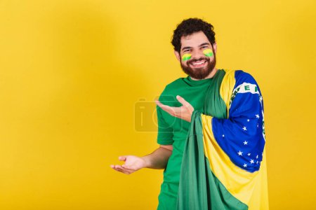 Photo for Caucasian man with beard, brazilian, soccer fan from brazil, presenting product with his hands, left. - Royalty Free Image