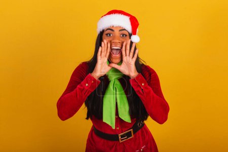 Photo for Beautiful black Brazilian woman, dressed in christmas clothes, santa claus, shouting promotion. - Royalty Free Image