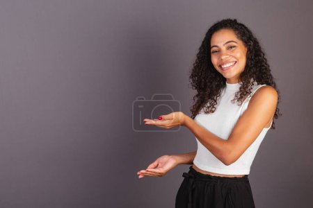 Photo for Young Brazilian black woman presenting with her hands to the left, publicity photo. - Royalty Free Image