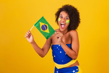 Téléchargez les photos : Jeune femme noire fan de football brésilien. tenant le drapeau brésilien - en image libre de droit
