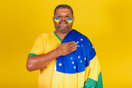 Foto de Hombre negro brasileño, fanático del fútbol de Brasil. con la mano en el pecho, cantando el himno nacional. democracia. - Imagen libre de derechos