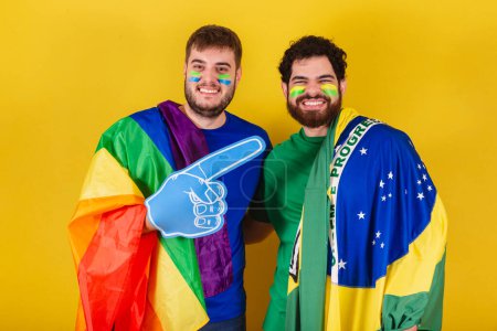 Foto de Pareja de hombres, brasileños, aficionados al fútbol de Brasil, con bandera LGBT - Imagen libre de derechos