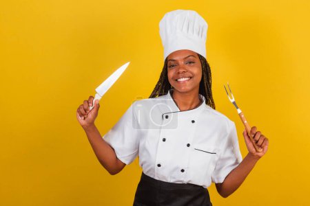 Photo for Young afro brazilian woman, chef cook, holding knife and fork for barbecue, getting ready to cook. - Royalty Free Image