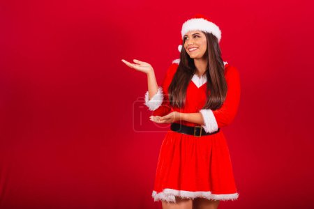 Foto de Hermosa mujer brasileña vestida con ropa de Navidad, Santa Claus. mostrando algo a la izquierda. - Imagen libre de derechos