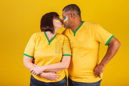 Photo for Couple, red-haired woman and black man, Brazilian soccer fans. giving kiss. - Royalty Free Image
