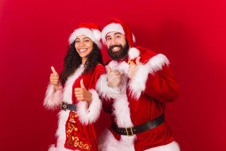 Photo for Brazilian couple, dressed for christmas, santa claus, mummy claus. like with hands, liked, approved, black woman and caucasian man. - Royalty Free Image