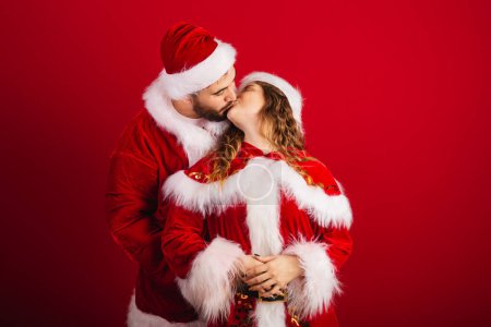Photo for Brazilian couple, dressed in Christmas clothes, Santa Claus, hugging, giving kiss - Royalty Free Image