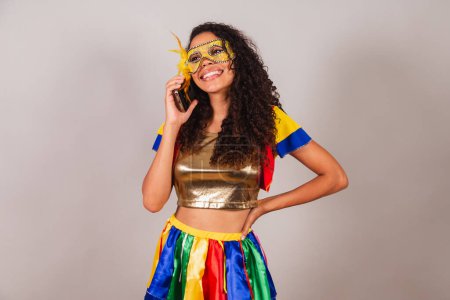 Téléchargez les photos : Belle femme brésilienne noire, portant des vêtements de carnaval, sur appel vocal avec smartphone. - en image libre de droit
