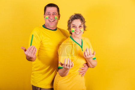 Photo for Adult couple, soccer fans from Brazil, calling with their hands, welcome, inviting. - Royalty Free Image