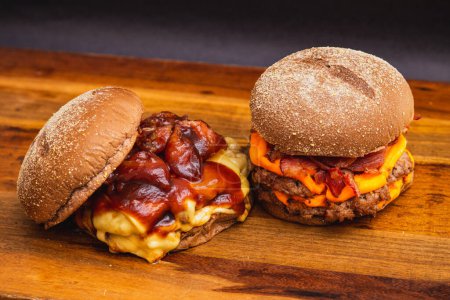 Photo for Two handmade burgers on a wooden board, made with beef. Bacon, cheese and barbecue sauce. - Royalty Free Image