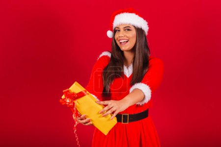 Foto de Hermosa mujer brasileña vestida con ropa de Navidad, Santa Claus. entrega de regalo amarillo. - Imagen libre de derechos