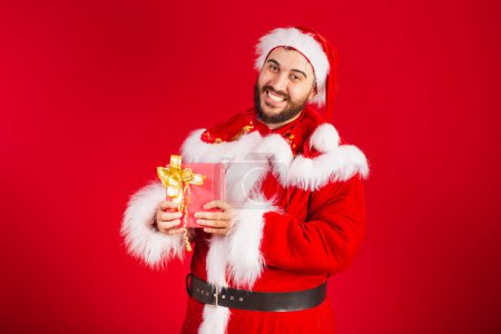 Photo for Brazilian man, dressed in santa claus clothes, holding red gift. - Royalty Free Image