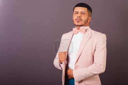 Photo for Brazilian black man, with pink suit and bow tie, gray background, holding suit - Royalty Free Image