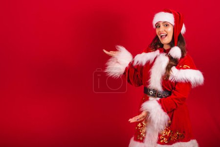 Foto de Mujer brasileña vestida con ropa de Navidad, Santa Claus. mostrando algo a la izquierda. - Imagen libre de derechos