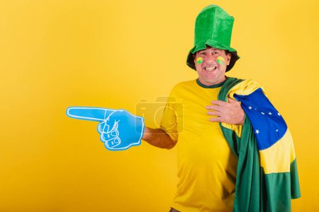 Photo for Adult man, soccer fan from brazil, wearing flag, with foam finger pointing left. - Royalty Free Image