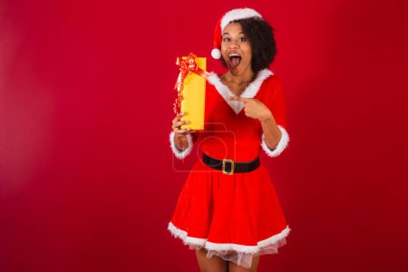 Photo for Beautiful black brazilian woman, dressed as santa claus, mama claus, pointing at gift - Royalty Free Image