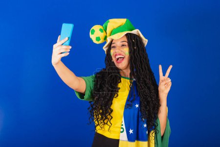 Téléchargez les photos : Jeune Brésilien noir, fan de foot. autoportrait en selfie, smartphone. - en image libre de droit