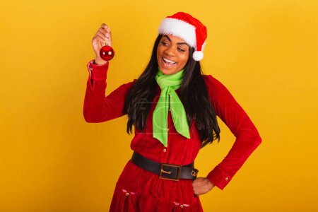 Photo for Beautiful black Brazilian woman, dressed in christmas clothes, santa claus, holding red ball, christmas decoration. - Royalty Free Image