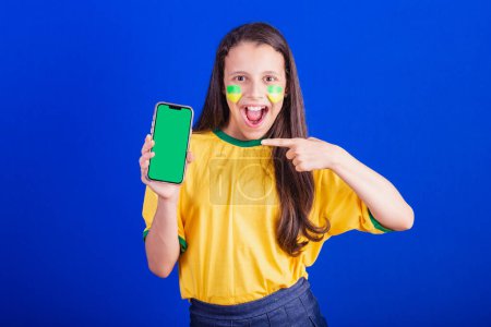 Photo for Young girl, soccer fan from Brazil. holding cellphone, screen for advertisement, promotion. Smartphone. applications. - Royalty Free Image