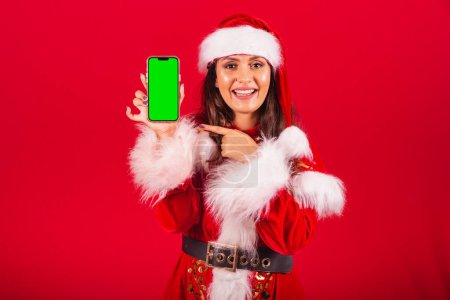 Photo for Brazilian woman dressed in Christmas clothes, Santa Claus. holding smartphone with green screen in chroma. - Royalty Free Image