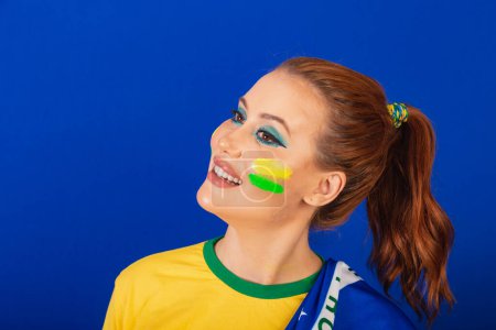 Téléchargez les photos : Femme caucasienne, rousse, fan de foot du Brésil, Brésilien, fond bleu, gros plan souriant avec visage peint - en image libre de droit