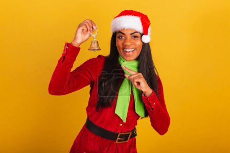 Foto de Hermosa mujer brasileña negra, vestida con ropa de Navidad, santa claus, sosteniendo la campana de Navidad. - Imagen libre de derechos