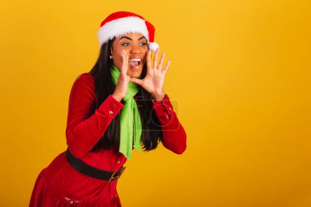 Foto de Hermosa mujer brasileña negra, vestida con ropa de Navidad, santa claus, gritando promoción. - Imagen libre de derechos