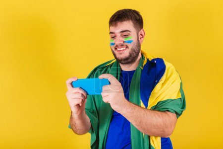 Photo for Brazilian caucasian man, soccer fan from Brazil, watching soccer match by smartphone, cellphone. - Royalty Free Image