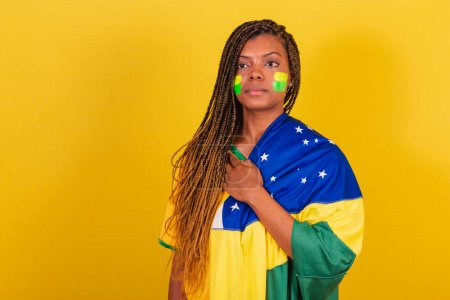 Foto de Mujer negra joven aficionada al fútbol brasileño. usando la bandera, cantando himno nace. - Imagen libre de derechos