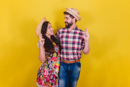 Photo for Beautiful couple dressed in typical clothes for a Festa Junina. Arraia de Sao Joao. Fingers crossed, cheering, wishing, luck concept. - Royalty Free Image