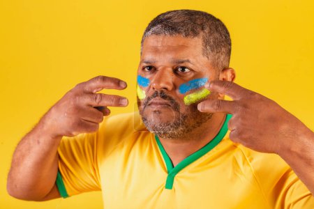 Foto de Hombre negro brasileño, fanático del fútbol de Brasil. foto de cerca, la aplicación de pintura facial, preparándose para el partido, la competencia. - Imagen libre de derechos