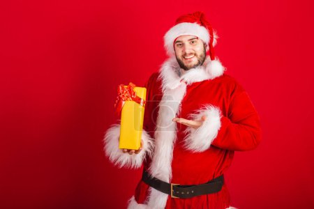 Foto de Caucásico, brasileño vestido con traje de Navidad, Santa Claus. sosteniendo regalo amarillo. - Imagen libre de derechos
