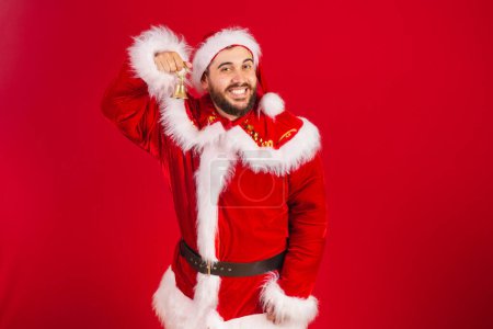 Foto de Hombre brasileño, vestido con ropa de Santa Claus, sosteniendo la campana de Navidad. - Imagen libre de derechos