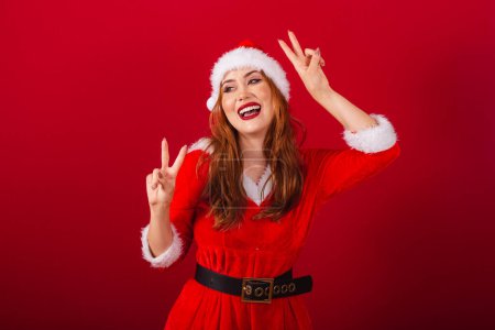 Téléchargez les photos : Belle femme rousse brésilienne, vêtue de vêtements de Noël, le Père Noël. paix et amour, posant pour la photo. - en image libre de droit