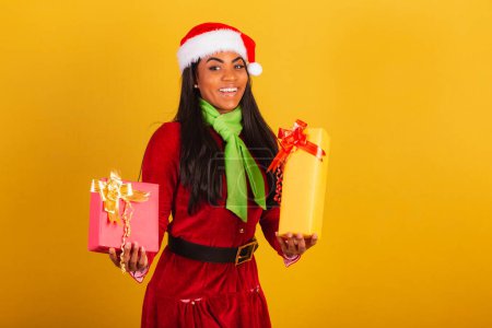 Photo for Beautiful black Brazilian woman, dressed in Christmas clothes, Santa Claus, holding two gifts. - Royalty Free Image